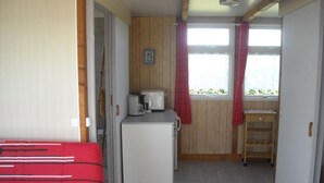 Una stanza compatta con un letto, un angolo cottura attrezzato con frigorifero, macchina del caffè e una finestra con tende.
