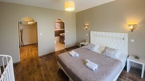 Ein Hotelzimmer mit einem großen Bett, einem Nachttisch, einer Lampe und Blick auf das Badezimmer und die Küche.