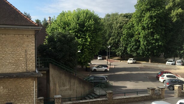 Um estacionamento com vários carros, um edifício com fachada de pedra e uma escadaria que leva a um nível superior.