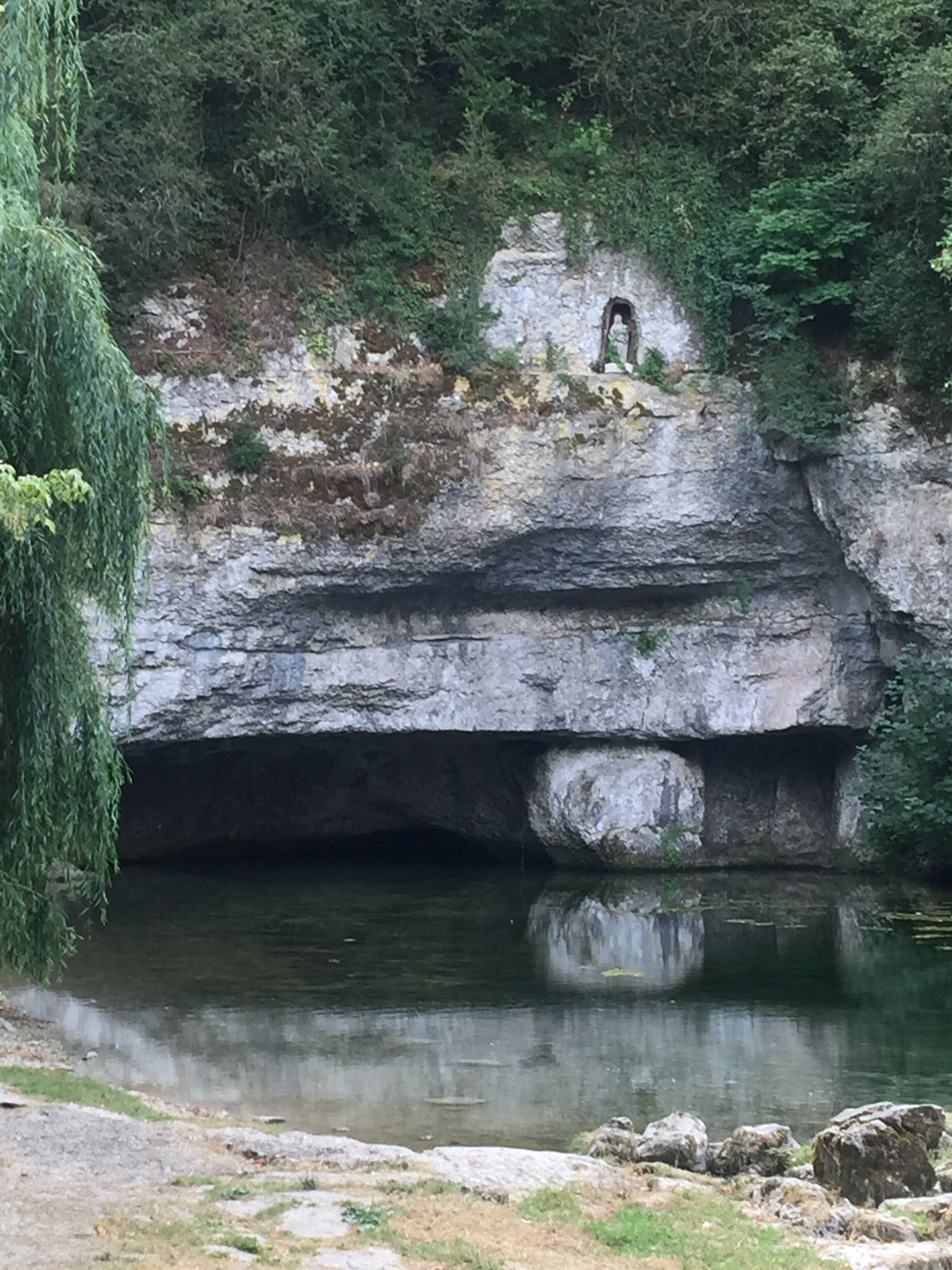 Une formation rocheuse naturelle dotée d’une entrée de grotte et d’une étendue d’eau qui reflète la structure.