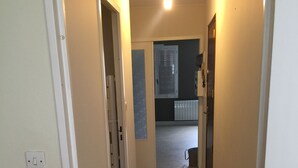 Um corredor estreito com piso de carpete, paredes brancas e luminária no teto.