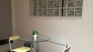 Uma pequena área de refeições com uma mesa de vidro e duas cadeiras de metal. Há uma planta em vaso sobre a mesa.