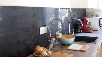 Une cuisine moderne avec une plaque de cuisson noire, un plan de travail en bois, un évier et une horloge au mur.