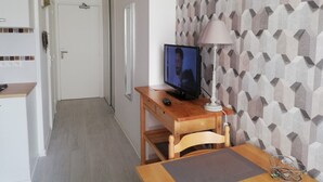A small room with a wooden desk, a television, and a lamp. There is a door in the background and a patterned wall. - very nice studio DINARD / LA RICHARDAIS 5 minutes from the beach (LA RICHARDAIS)