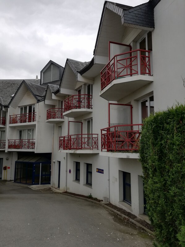 A multi-story building with balconies, a parking sign, and a gated entrance.