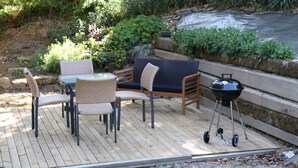 Eine Holzterrasse mit Gartenmöbeln, darunter ein Tisch, Stühle und ein Grill.