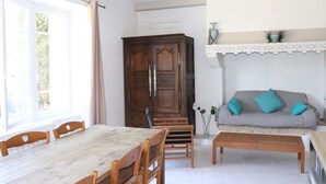 Ein Zimmer mit einem Holzespeisetisch, Stühlen, einer Couch mit türkisfarbenen Kissen, einer Holzschrank und einem Spitzenregal.