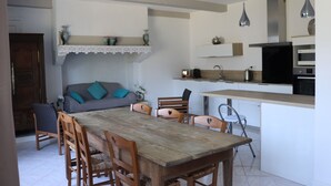 Ein Essbereich mit Holztisch und -stühlen, einer Couch mit türkisfarbenen Kissen sowie eine Küchenzeile mit modernen Geräten.