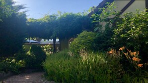A garden pathway leading to a building with a traditional architectural style, surrounded by lush greenery and flowering plants. - The lodge "L'Allée du Val" (Lalaye)