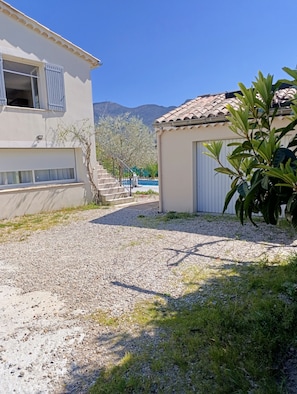 A residential area with a gravel driveway, a white building with a blue door, and a small structure with a tiled roof.
