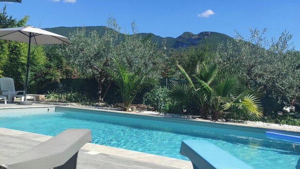 A swimming pool with lounge chairs and umbrellas, surrounded by greenery and mountains. - House with private pool and garden (Nyons)