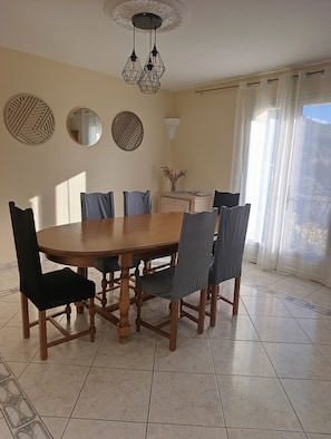 A dining area with a round wooden table, six chairs, decorative wall mirrors, and a ceiling light fixture.
