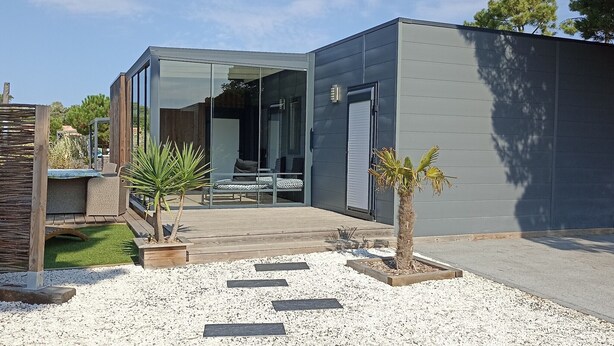 Une maison moderne avec une entrée dotée d’une porte en verre, une terrasse en bois et un petit jardin agrémenté de gravier et de dalles.
