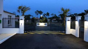 Une entrée fermée par un portail donne accès à une propriété, et une allée pavée mène à un bâtiment.