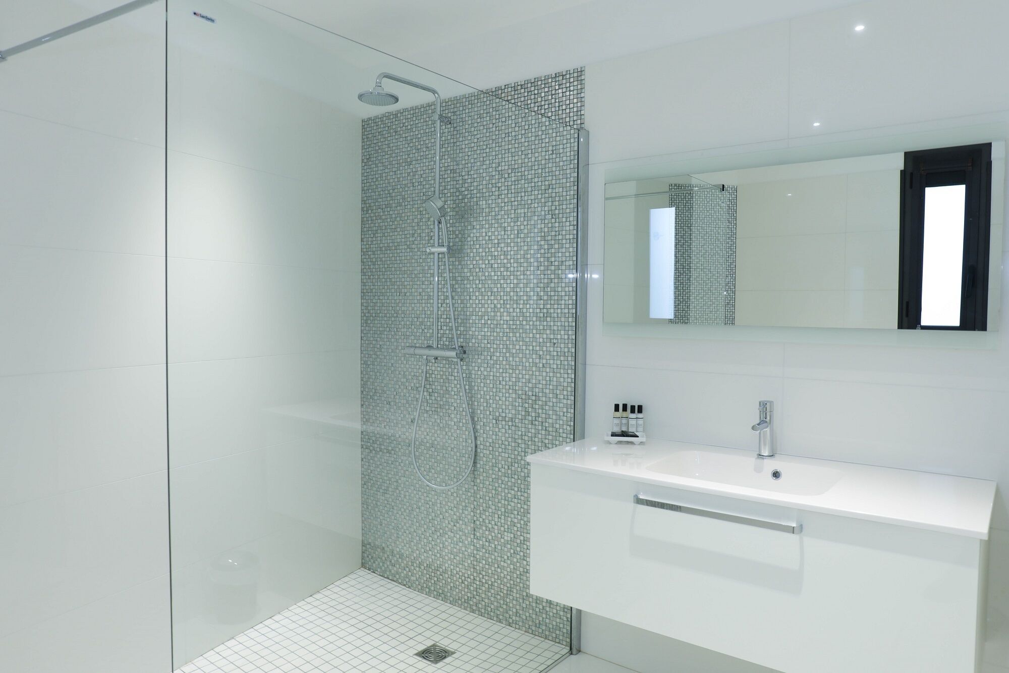 Un bany modern amb un box de dutxa de vidre, un lavabo blanc i un mirall sobre la petita taula.