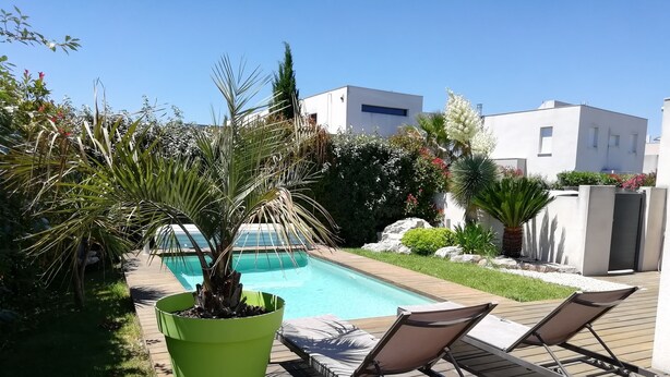 Zona de piscina amb gandules, una jardiniera verda i un edifici modern al fons.