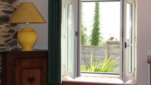 Ett fönster med en öppen fönsterlucka, en gul lampa och en grön gardin.