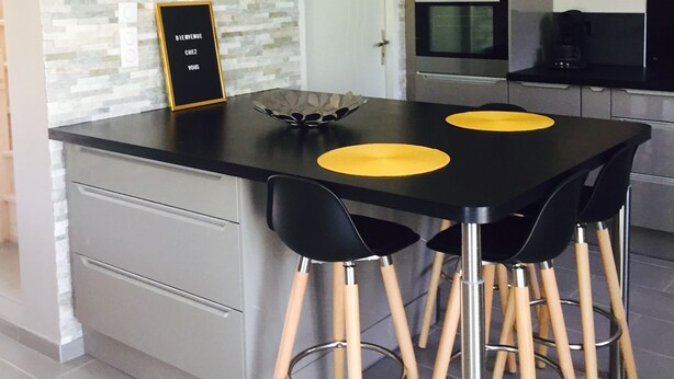 Une cuisine moderne avec un îlot central noir, deux sets de table jaunes et des chaises noires aux pieds en bois.
