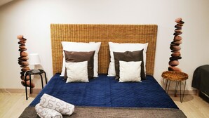Un lit avec une tête de lit en osier, deux oreillers, une couverture bleue et une serviette pliée.
