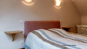 A bedroom with a bed, two wall-mounted lights, a small wooden shelf, and a window with a white blind. - ----- Ty Corentin ---- (LA FORET FOUESNANT,)