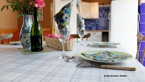 A dining table set with a floral tablecloth, a green bottle, and a vase with pink flowers. - ----- Ty Corentin ---- (LA FORET FOUESNANT,)
