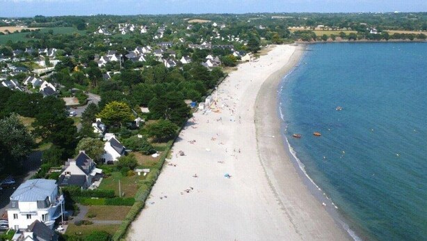 An aerial view of a coastal area with a sandy beach, houses, and a clear blue sea. - ----- Ty Corentin ---- (LA FORET FOUESNANT,)
