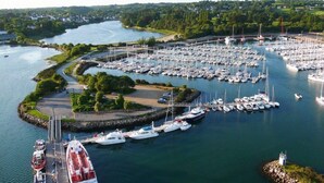 A marina with numerous boats docked, surrounded by greenery and a small island with a lighthouse. - ----- Ty Corentin ---- (LA FORET FOUESNANT,)