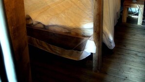 Una cama con dosel de madera con cuatro columnas, una mesita de noche con lámpara y suelo de madera.