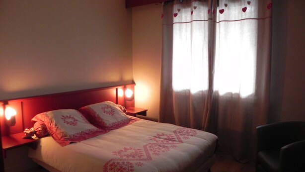 A bedroom with a bed, two bedside lamps, a chair, and a window with curtains. - At the heart of the resort Lioran (Laveissière)