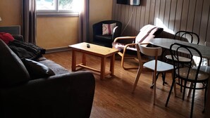 A modern living room with a wooden floor, a sofa, a table, and a TV mounted on the wall. - At the heart of the resort Lioran (Laveissière)