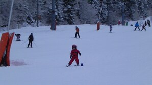 A ski slope with skiers and a child in red. - At the heart of the resort Lioran (Laveissière)