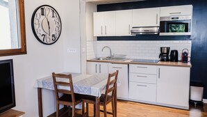 Una cocina moderna con armarios blancos, microondas y cafetera. Hay una mesa de comedor de madera con sillas y un reloj de pared grande.
