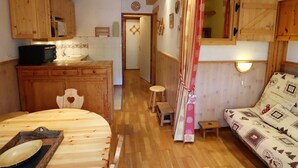 A cozy cabin interior with wooden beams, a dining table, a sofa, a kitchen area, and a small stool. - Functional apartment for 4-6 people with pool, TV, dishwasher and balcony in Arêches-Beaufort (Arêches-Beaufort)