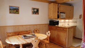 A wooden dining table with chairs, a kitchen area with wooden cabinets and a microwave, and two framed pictures on the wall. - Functional apartment for 4-6 people with pool, TV, dishwasher and balcony in Arêches-Beaufort (Arêches-Beaufort)