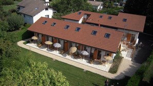 Un bâtiment à deux étages, doté d’un toit en pente, de nombreuses fenêtres et d’un espace extérieur aménagé avec des parasols.