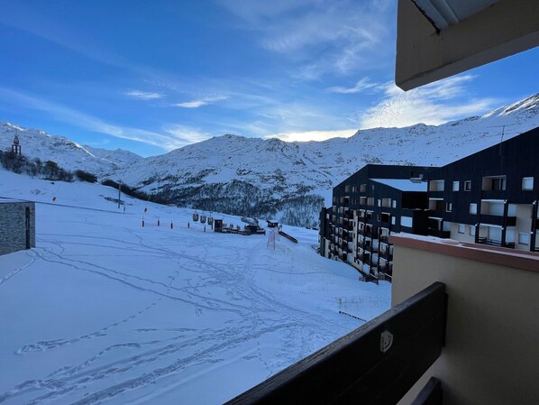 A snow-covered mountain landscape with a ski lift, a building with multiple balconies, and a clear sky.