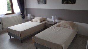 A twin room with two single beds, bedside tables with lamps, a radiator, and a window with curtains. - HARAS DU CROC MARIN Principal (Montigny-sur-Loing)