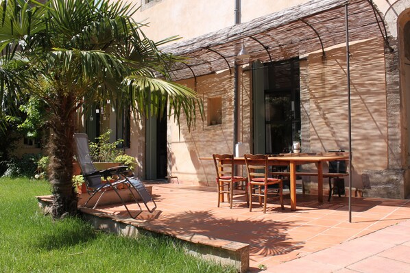 A patio with a table and chairs, a palm tree, and a building with a tiled roof.