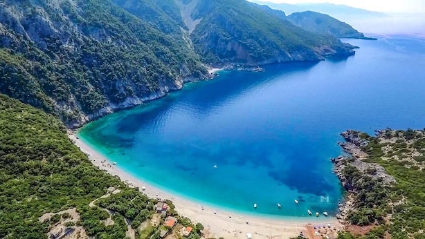 An aerial view of a coastal area with a clear blue sea, a sandy beach, and lush green hills. - Villa Serenity (Kymi-Aliveri)