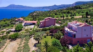 A coastal property with multiple buildings, including a pink house with a balcony and a red-roofed structure. - Villa Serenity (Kymi-Aliveri)