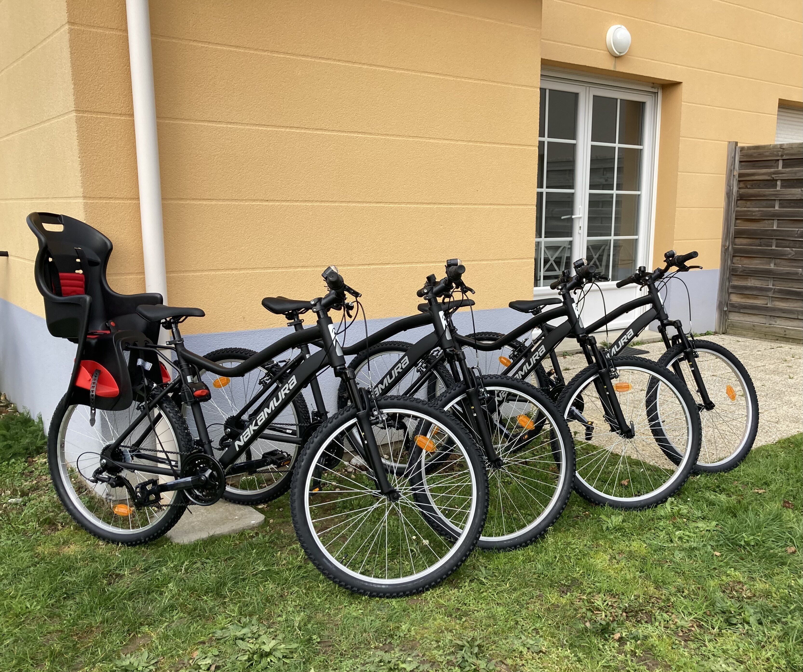 A row of bicycles parked against a building with a window and a door.