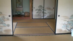 Una habitación tradicional japonesa con suelo de tatami, puertas correderas decoradas con motivos naturales y un pequeño estante con adornos.