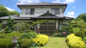 Una casa tradicional japonesa con tejado de tejas, puerta de madera y jardines cuidados.