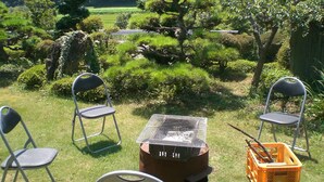 Un espacio al aire libre con césped y sillas de metal dispuestas alrededor de una parrilla.