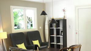 Een woonkamer met een bank, twee fauteuils, een salontafel, een boekenkast en een hanglamp.