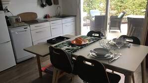 Een moderne keuken met witte apparaten, een eettafel gedekt voor twee personen en een uitzicht op de omgeving door een groot raam.