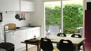 Een moderne keuken met witte kasten, een eettafel met stoelen en uitzicht op groen.