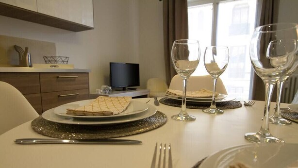 A dining table set with plates, cutlery, and wine glasses, with a television and a window in the background. - 🎖 Pretty 3 rooms in the city center (Annecy)