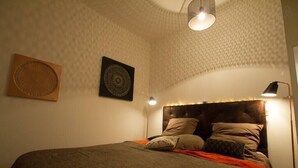 A neatly made bed with a dark headboard and multiple pillows, a wall-mounted circular light fixture, and a small table lamp beside the bed. - 🎖 Pretty 3 rooms in the city center (Annecy)