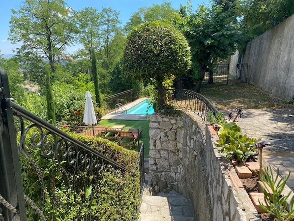 A stone staircase leading to a pool area surrounded by lush greenery and a stone wall.